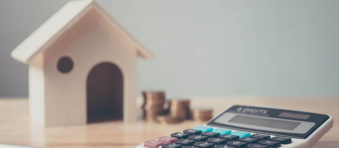 Calculator With Wooden House And Coins Stack And Pen On Wood Tab