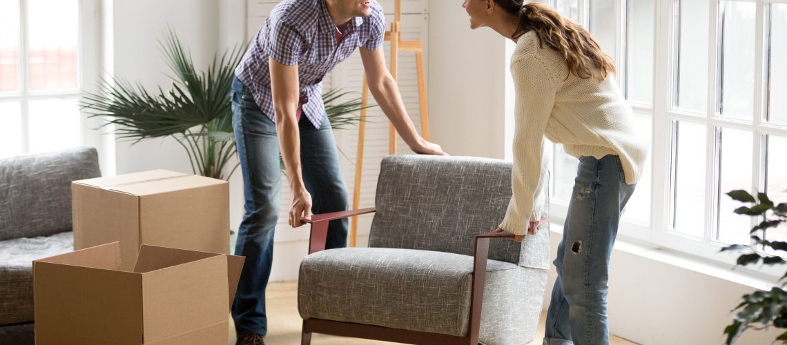 Smiling Couple Carrying Modern Chair Together Placing Furniture