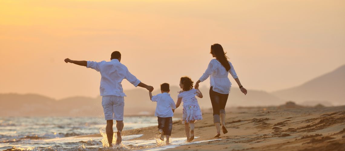 happy young family have fun on beach run and jump  at sunset